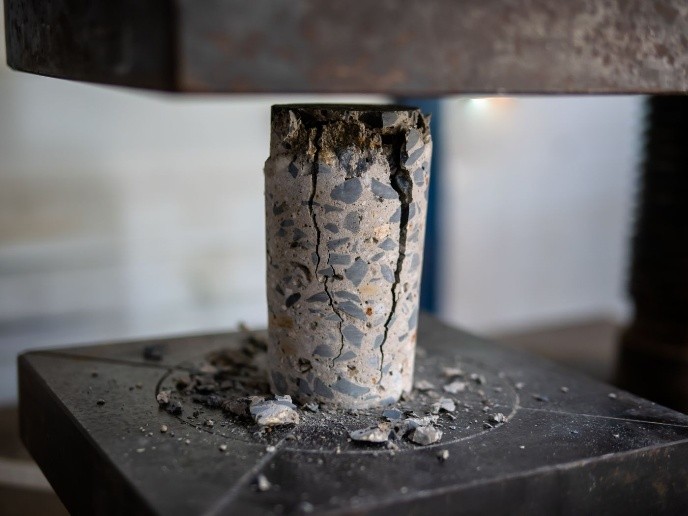 UCS testing machine applying axial load on cylindrical rock sample.
